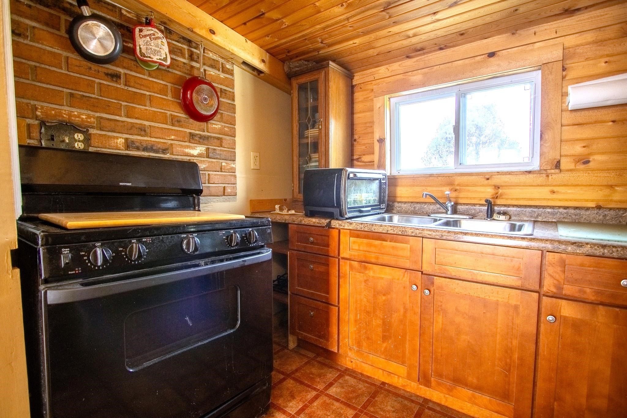 3946 East Calvary Road Duluth, MN 55803 - Photo 8 of 12 Kitchen with gas stove, brown cabinetry, wood ceiling, glass insert cabinets, and light countertops