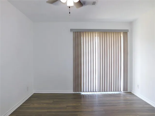 an empty room with wooden floor chandelier fan and windows