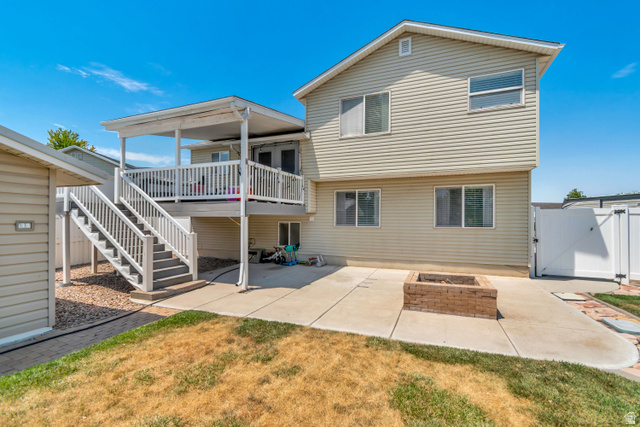 4752 South 4075th Street West Roy, UT 84067 - Photo 28 of 28 Rear exterior featuring a covered deck with white railings and dual staircases, a concrete patio, and a built-in brick fire pit