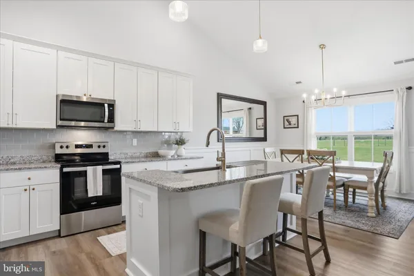 a kitchen with stainless steel appliances granite countertop a stove a sink a microwave a dining table and chairs with wooden floor
