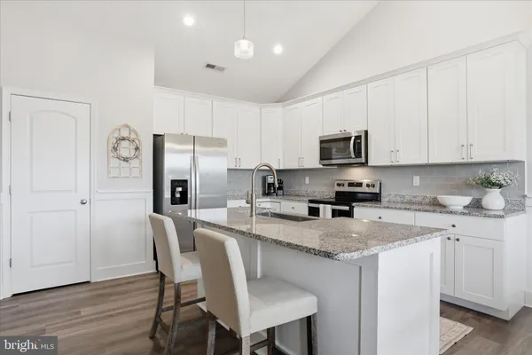 a kitchen with stainless steel appliances granite countertop a stove a sink a microwave a refrigerator white cabinets and wooden floor