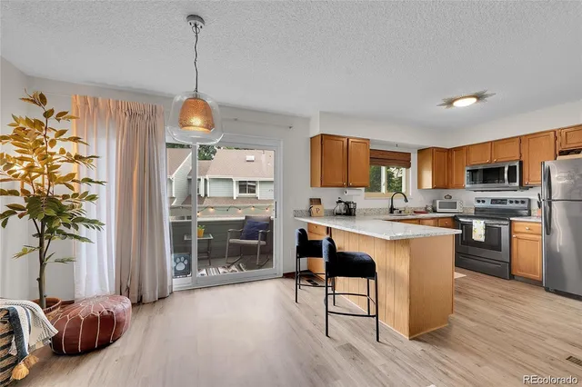 a kitchen with stainless steel appliances granite countertop a refrigerator a sink dishwasher a stove and a dining table with wooden floor