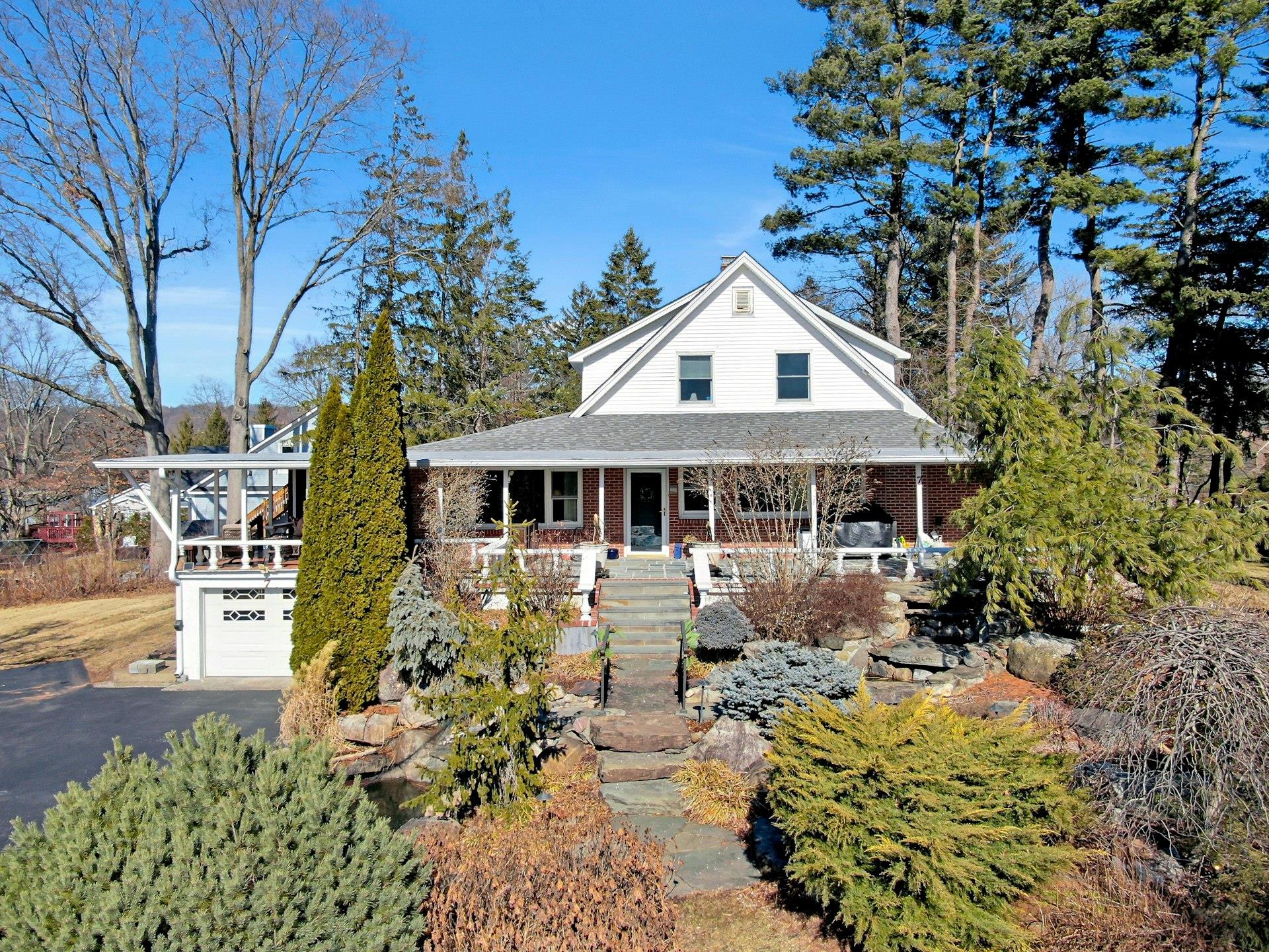 Farmhouse with stairway, an attached garage, aphalt driveway, brick siding, and a porch