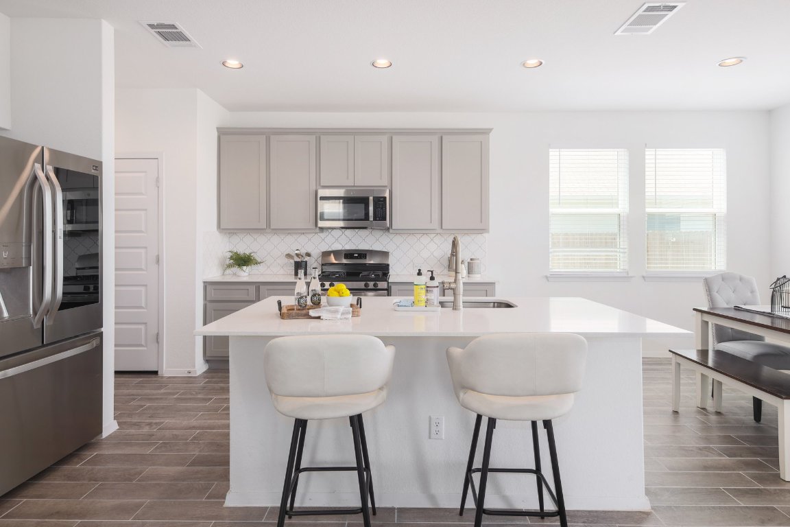 1408 Flint Knapper Drive Georgetown, TX 78626 - Photo 12 of 32 a kitchen with stainless steel appliances a sink a stove a refrigerator cabinets and a dining table with wooden floor
