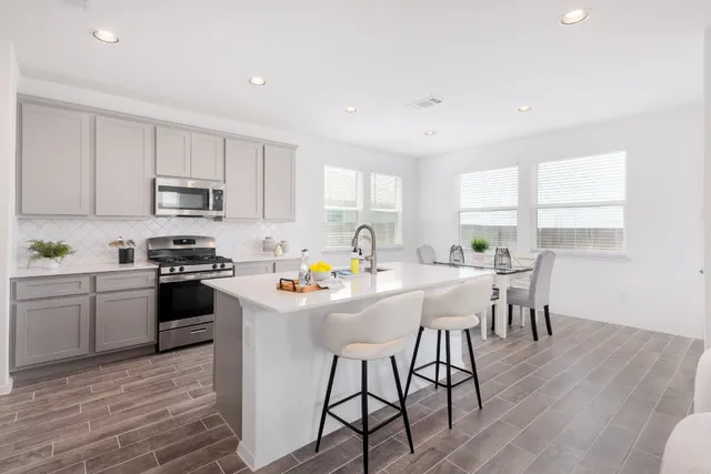 a kitchen with stainless steel appliances a stove a sink a refrigerator white cabinets and wooden floor