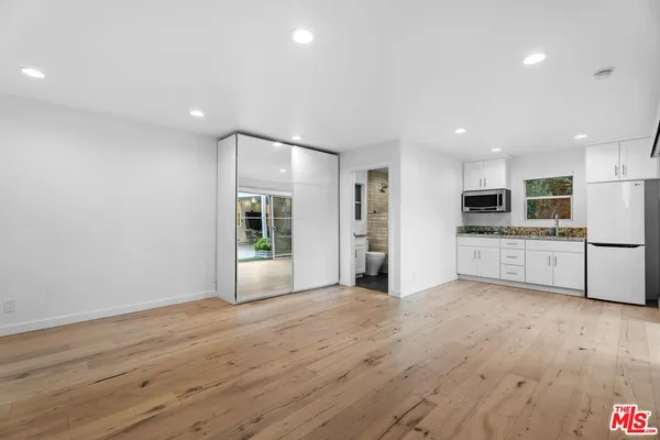a view of an empty room with wooden floor and kitchen