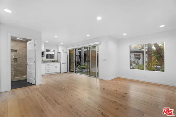 a view of an empty room with wooden floor and a kitchen