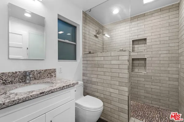 a bathroom with a granite countertop toilet a sink a mirror and shower