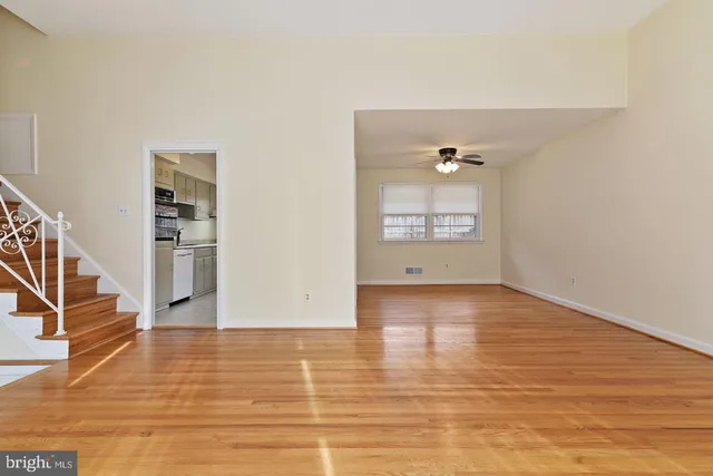 a view of empty room with wooden floor and kitchen