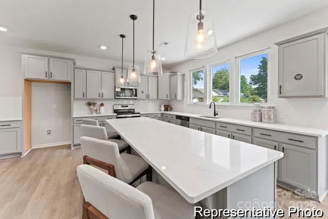 a large kitchen with cabinets a sink a center island stainless steel appliances and a window