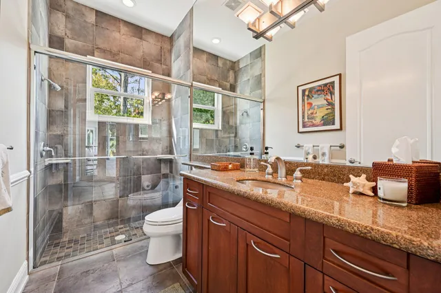 a bathroom with a granite countertop sink a toilet a mirror and shower