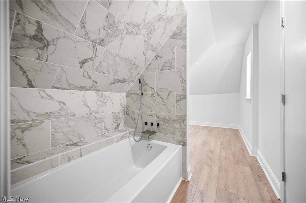28300 Aurora Road Solon, OH 44139 - Photo 24 of 36 Bathtub with marble-patterned tile surround and a handheld shower fixture