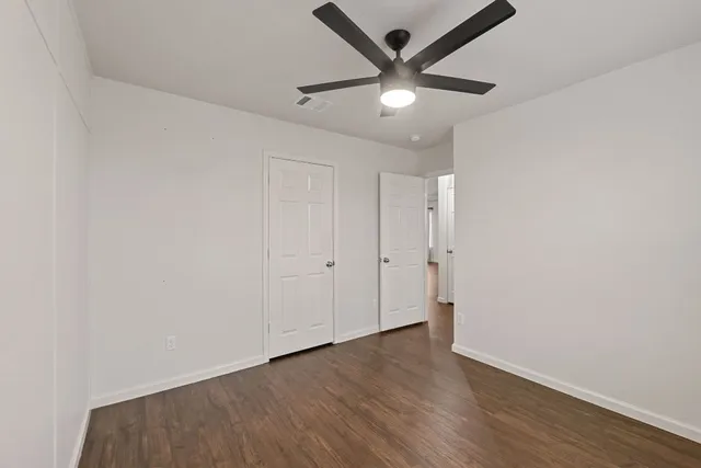 an empty room with wooden floor fan and windows