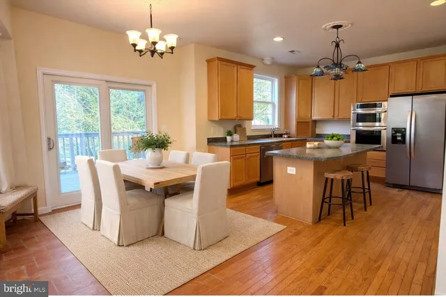 a dining hall with stainless steel appliances granite countertop a stove a refrigerator a kitchen island a dining table and chairs