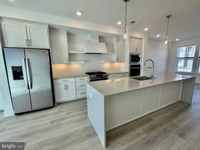 a kitchen with stainless steel appliances granite countertop a sink a refrigerator a microwave a stove and white cabinets with wooden floor