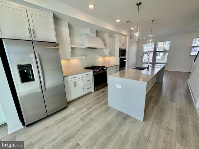 a large kitchen with stainless steel appliances granite countertop a refrigerator a sink a stove a microwave a island and white cabinets with wooden floor