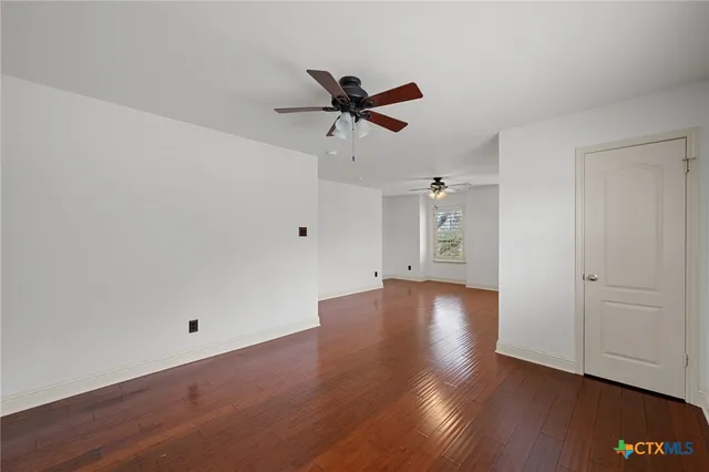 an empty room with wooden floor ceiling fan and windows