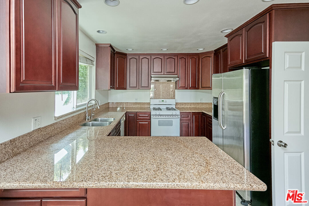 1253 Keniston Avenue Los Angeles, CA 90019 - Photo 10 of 35 a kitchen with stainless steel appliances granite countertop a refrigerator a stove and a sink with wooden cabinets