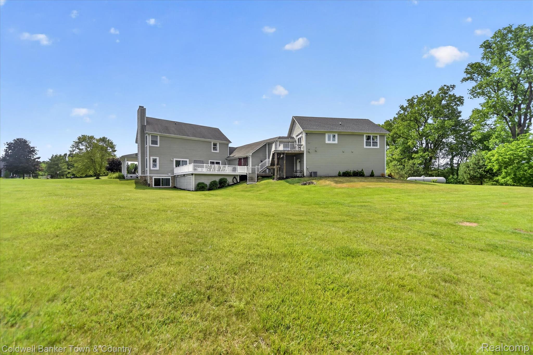 918 Gray Fox Court Howell, MI 48843 - Photo 67 of 84 Expansive green lawn bordering a light gray siding residence with multiple levels, featuring a white deck with railings and mature perimeter trees
