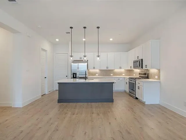 a kitchen with stainless steel appliances kitchen island granite countertop a stove a sink a refrigerator and white cabinets with wooden floor