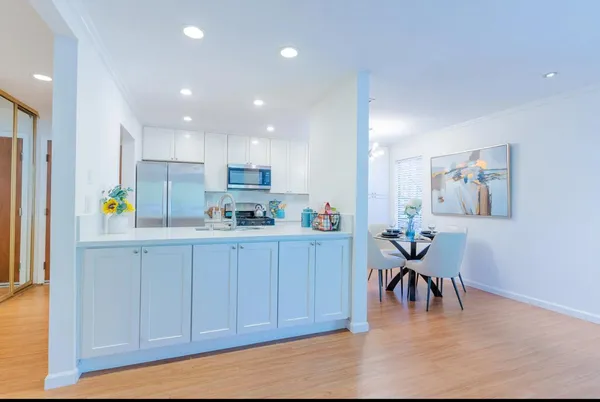 a kitchen with stainless steel appliances granite countertop a refrigerator a stove a dining table and chairs with wooden floor