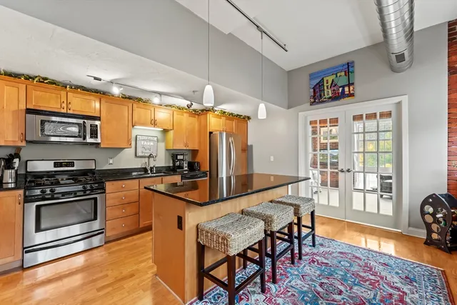 a kitchen with stainless steel appliances granite countertop a stove top oven a refrigerator a dining table and chairs with wooden floor