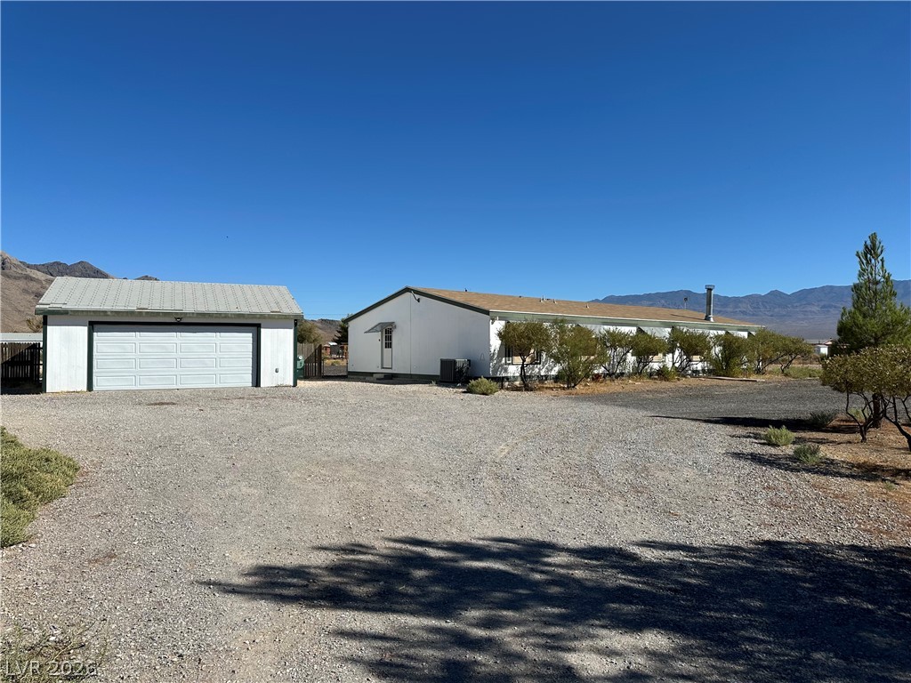 3270 West Simkins Road Pahrump, NV 89060 - Photo 2 of 36 An expansive gravel driveway leads past a detached garage toward the main residence.