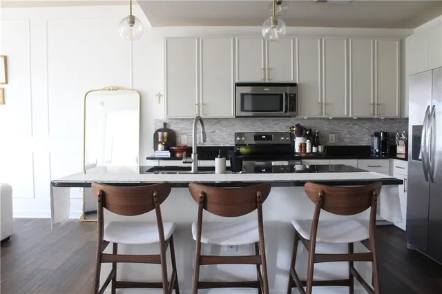 a kitchen with stainless steel appliances granite countertop a sink a stove a kitchen island with chairs and white cabinets