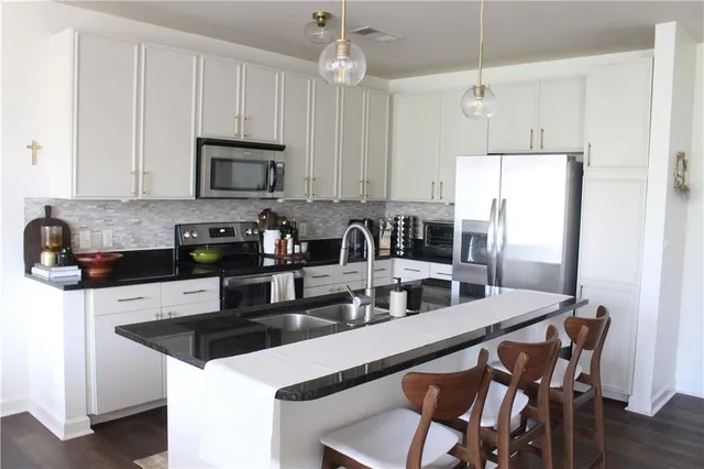 a kitchen with stainless steel appliances granite countertop a stove a sink a microwave a refrigerator and white cabinets