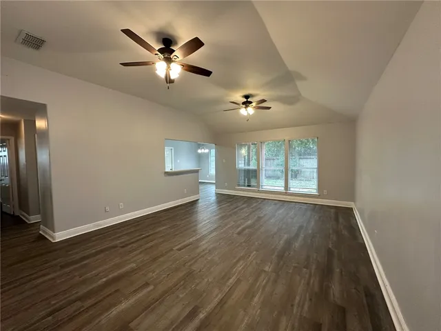 an empty room with wooden floor chandelier fan and windows