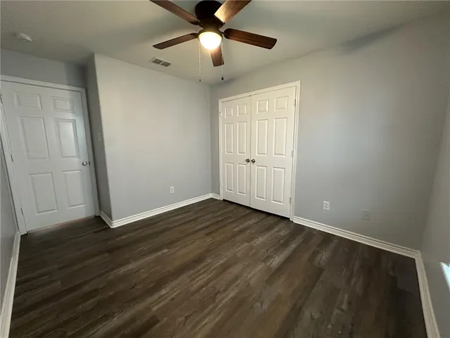 a view of an empty room with wooden floor and a ceiling fan