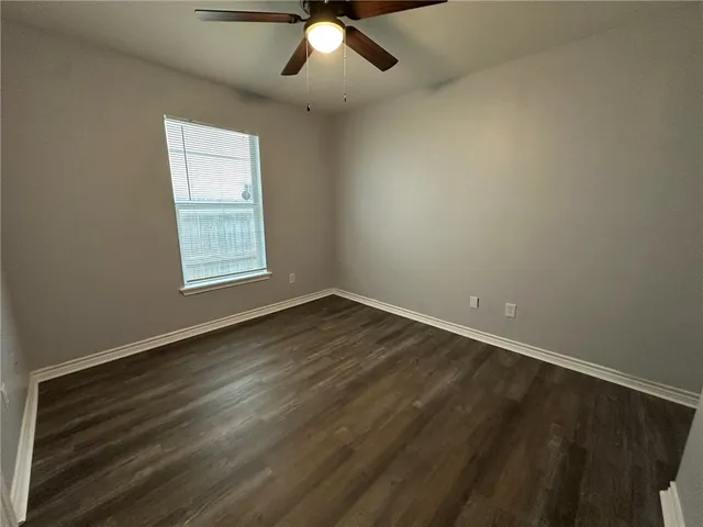 an empty room with wooden floor chandelier fan and windows