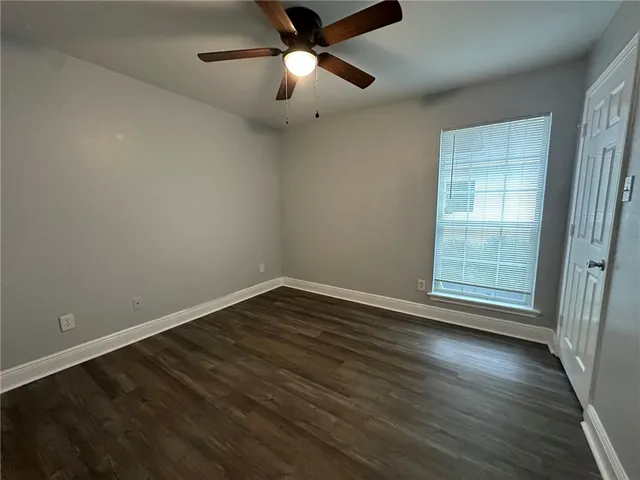 an empty room with wooden floor fan and windows