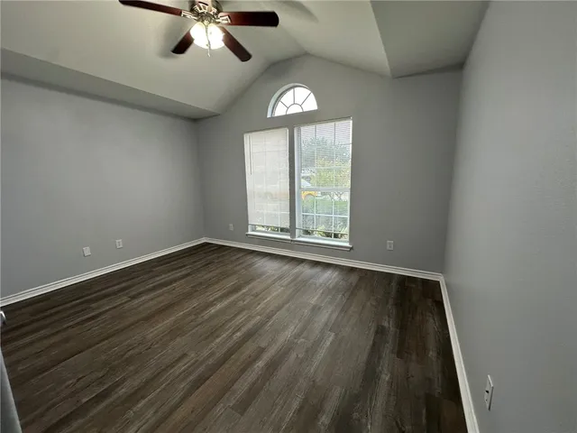an empty room with wooden floor chandelier fan and windows