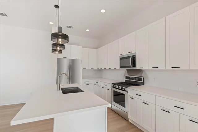 a kitchen with stainless steel appliances kitchen island granite countertop a stove a sink a refrigerator white cabinets and wooden floor