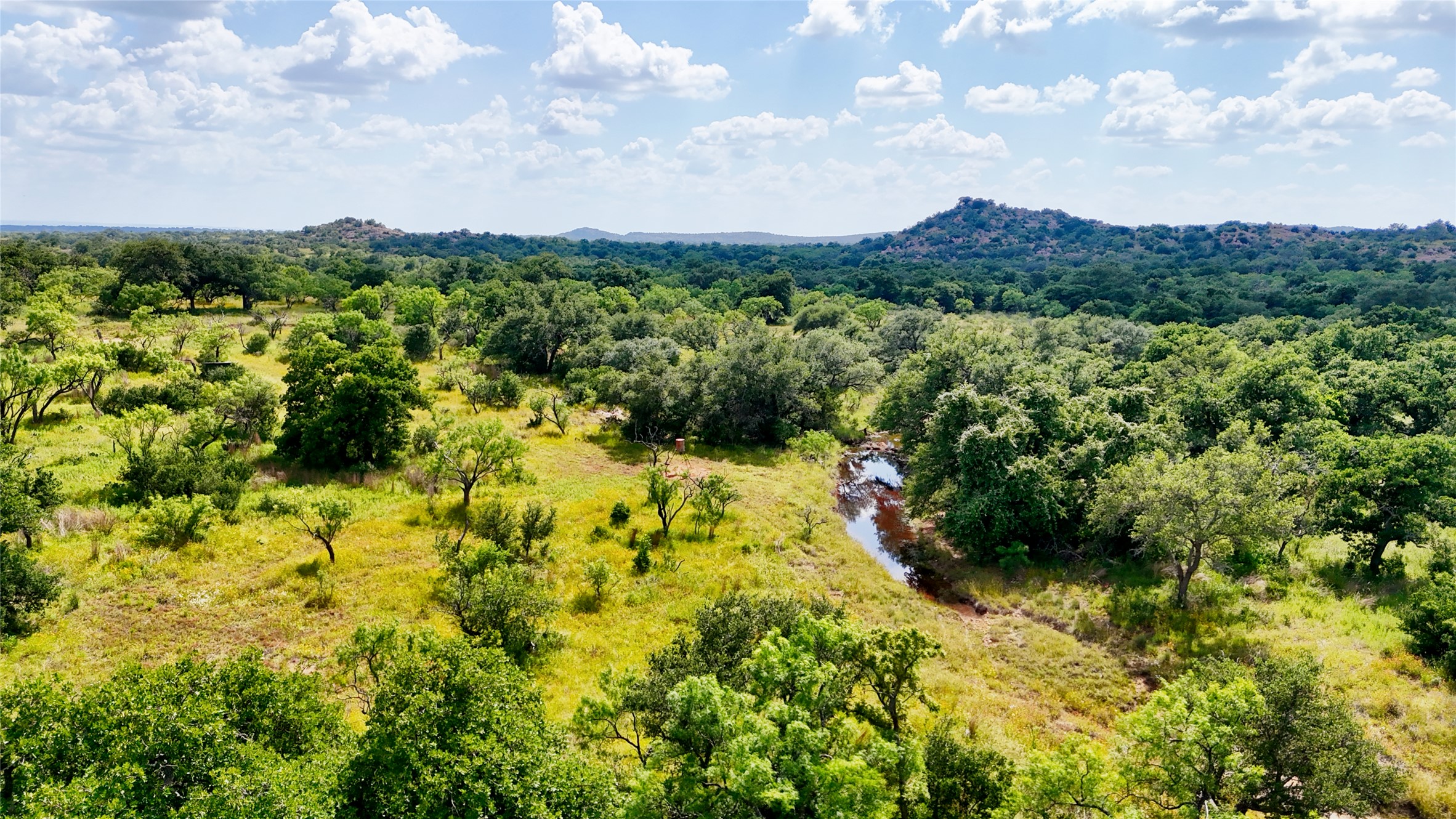 Vast natural acreage featuring a winding creek and distant hills under an open sky.
