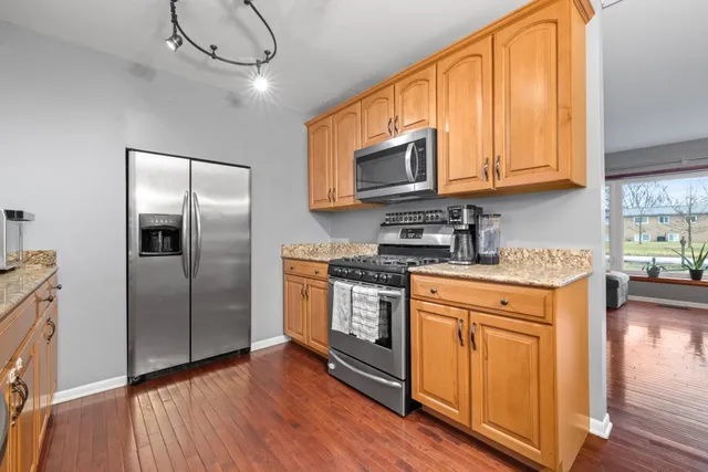 a kitchen with stainless steel appliances granite countertop a refrigerator a microwave oven a sink with wooden floors and cabinets