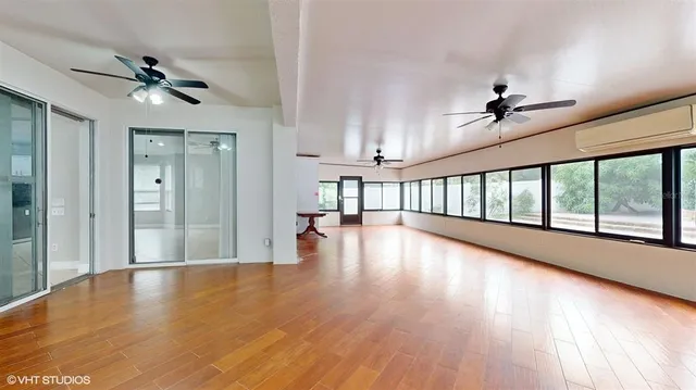 a view of an empty room with wooden floor fan and windows