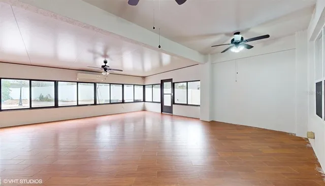 an empty room with wooden floor chandelier ceiling fan and windows