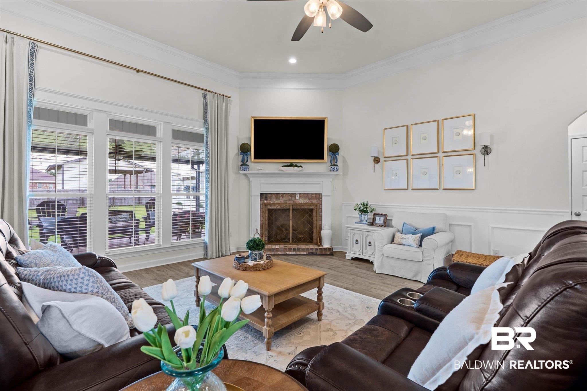 9074 Moses Way Theodore, AL 36582 - Photo 14 of 52 Spacious living area featuring large windows, a ceiling fan, a fireplace with a brick surround, wood-finish flooring, and crown molding