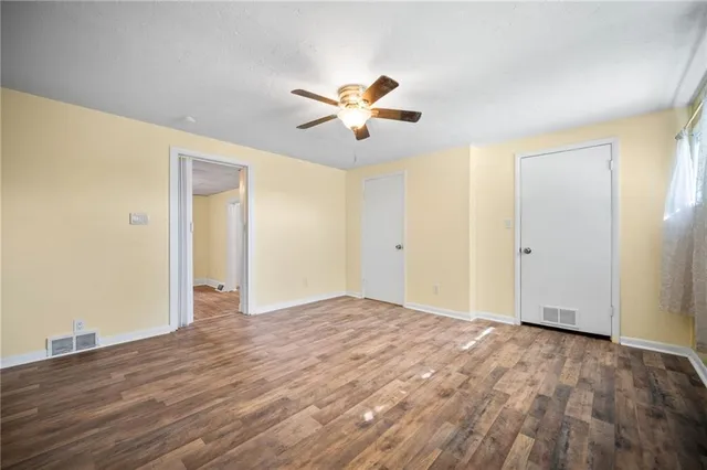 an empty room with wooden floor fan and windows