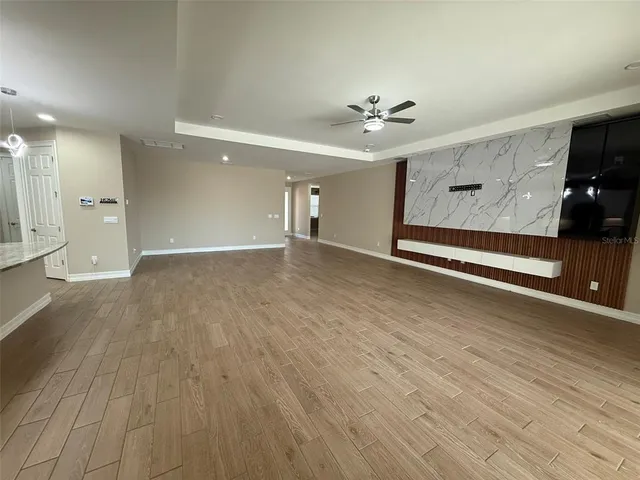 an empty room with wooden floor chandelier fan and windows