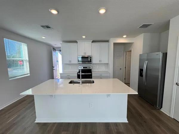a kitchen with stainless steel appliances a refrigerator a stove a sink a microwave and white cabinets with wooden floor