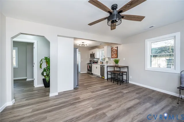 a living room with stainless steel appliances furniture wooden floor and a view of kitchen
