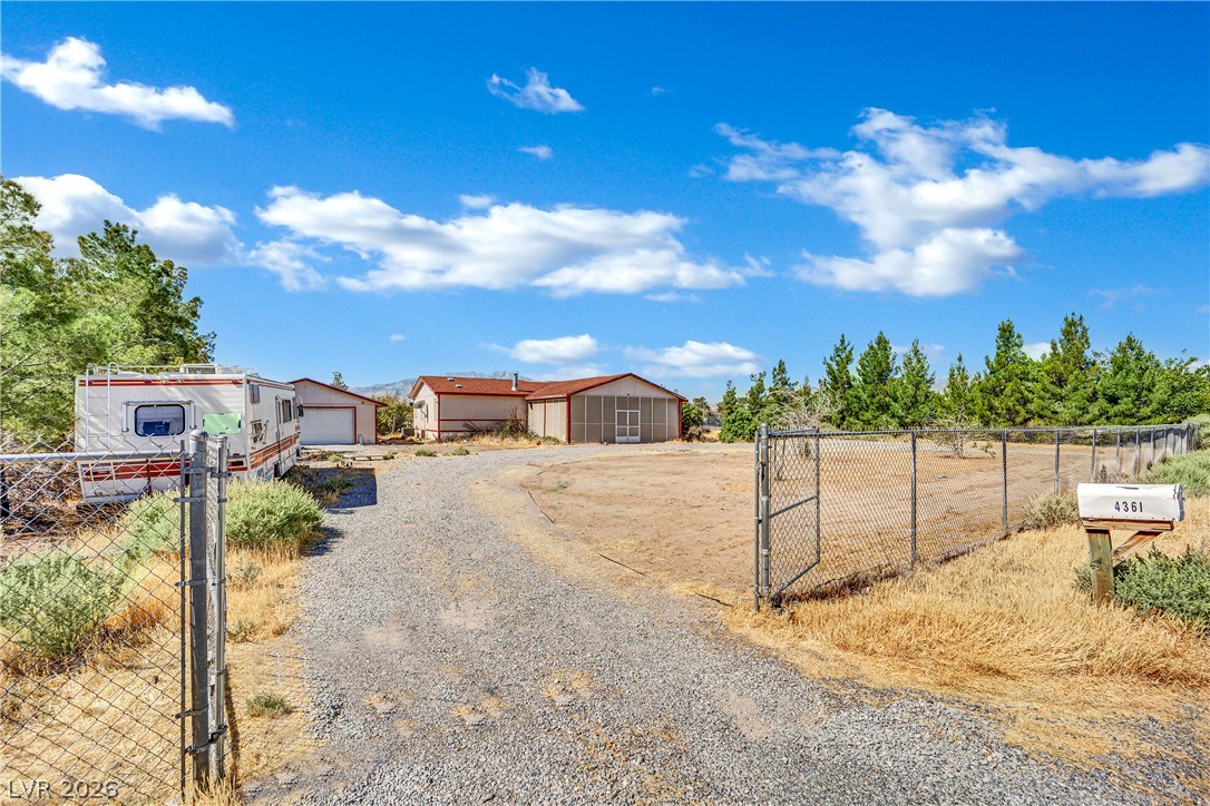 4361 Maple Road Pahrump, NV 89048 - Photo 4 of 46 A spacious gravel driveway leads to a secluded residence, bordered by natural landscaping.