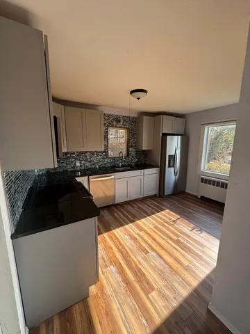 a living room with a couch wooden floor and kitchen view