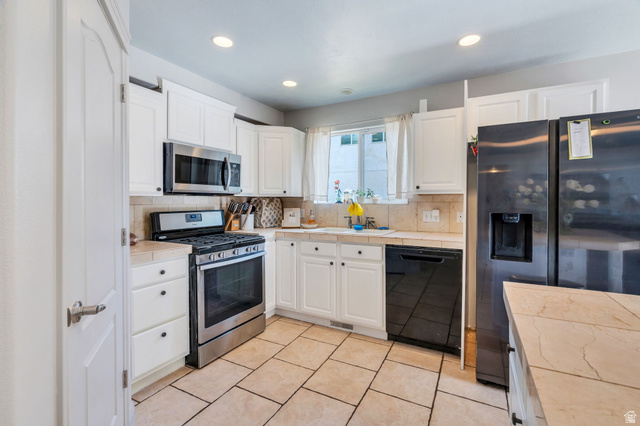 1727 South Sandhill Road Orem, UT 84058 - Photo 8 of 27 Kitchen featuring white cabinetry with black hardware, stainless steel appliances, beige tile flooring, and light-toned countertops