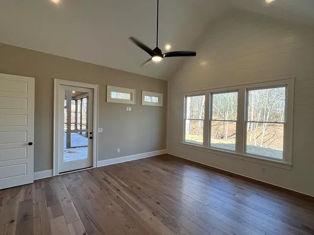 a view of an empty room with wooden floor and fan