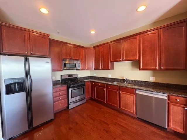 a kitchen with stainless steel appliances granite countertop wooden cabinets a stove a sink and a refrigerator