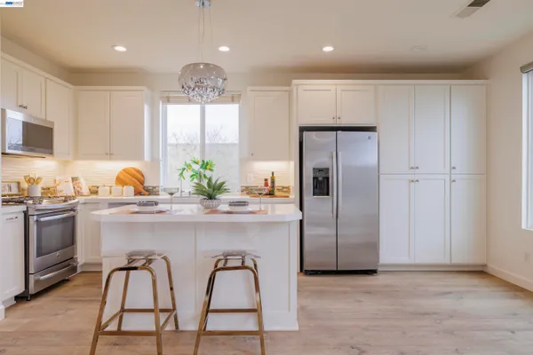 a large white kitchen with stainless steel appliances granite countertop a stove a sink dishwasher a dining table and chairs with wooden floor
